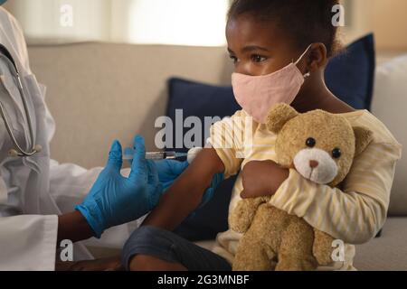 Une femme afro-américaine donne la vaccination contre le covid à une jeune patiente dans un masque facial à la maison Banque D'Images