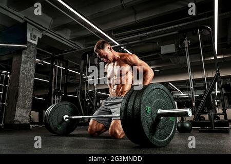 Atelt avec un corps magnifiquement sculpté se prépare à faire des exercices avec une barbell. L'athlète prépare la barbell pour l'entraînement des muscles. Sports i Banque D'Images