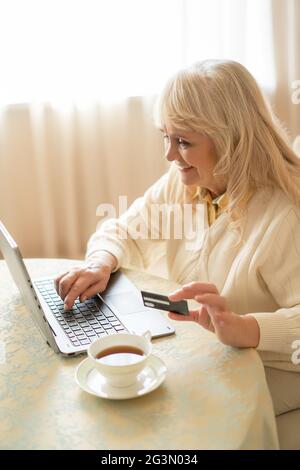 Femme âgée faisant des achats sur Internet tout en étant assise à la table Banque D'Images