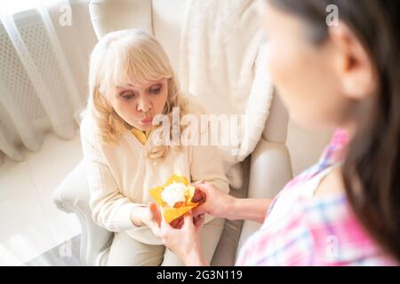 Charmante fille donne un petit gâteau d'anniversaire avec bougie à sa mère âgée Banque D'Images