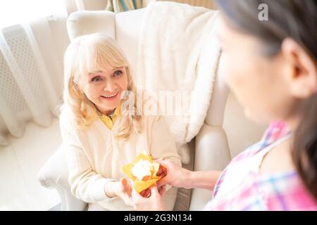 Charmante fille donne un petit gâteau d'anniversaire avec bougie à sa mère âgée Banque D'Images