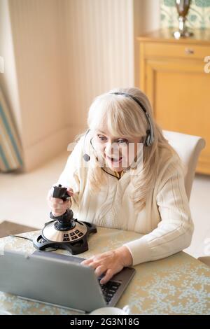 Une femme âgée joue à des jeux vidéo avec un joystick sur un ordinateur portable Banque D'Images