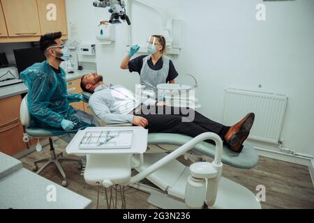 Mâle caucasien allongé sur un lit pliant assis avec des médecins tout en examinant l'intérieur de la bouche