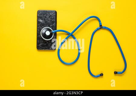 Le concept de l'assistance technique pour la panne du smartphone. Écran en verre cassé d'un smartphone, stéthoscope sur fond jaune Banque D'Images