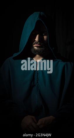 Un africain musulman avec une barbe priant dans un endroit sombre et porte un bleu traditionnel marocain djellaba. Banque D'Images