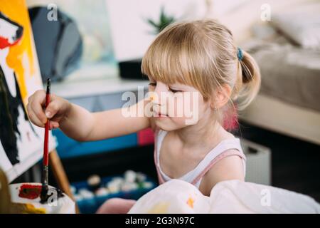 Une petite fille mignonne peint une grande image avec de l'acrylique à la maison sur un chevalet. Banque D'Images