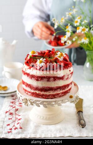 Gâteau de velours rouge avec fraise, crème fouettée et bouquet de pâquerettes sur tableau blanc sur fond gris. Saint-Valentin, dessert de mariage ou anniversaire p Banque D'Images