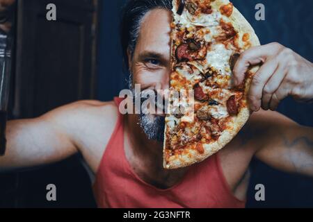 Homme barbu brutal à la maison Manger une pizza et boire de l'alcool. Banque D'Images