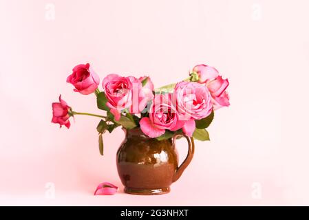 Belles roses sur fond rose dans un vase en céramique brun Banque D'Images