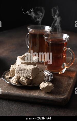 Halva doux et thé chaud dans des tasses en verre sur fond brun foncé. Orientation verticale. Gros plan. Banque D'Images
