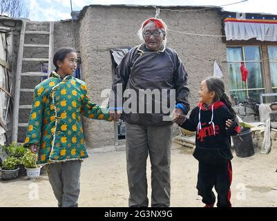 (210617) -- LHASSA, le 17 juin 2021 (Xinhua) -- Sonam, main dans la main avec deux de ses grandes petites-filles, va faire une promenade au village de Xaga, canton d'EMA, comté de Namling, ville de Xigaze, région autonome du Tibet du sud-ouest de la Chine, le 18 avril 2021. Sonam, 86 ans, résidant du village de Xaga, a commencé à travailler dur lorsqu'il avait 13 ans dans un manoir local, où, outre la garde des enfants du propriétaire du manoir, il a dû grader les animaux pendant la journée et les garder nourris pendant la nuit. Il lui-même, cependant, n'avait pas suffisamment de nourriture et de vêtements, et a été forcé de dormir avec les animaux au niveau de la bergerie. 'J'ai eu b Banque D'Images