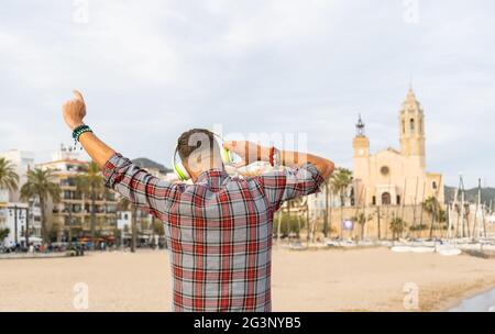 Un homme heureux et enthousiaste avec des bras levés pour écouter de la musique avec des écouteurs sur la plage Banque D'Images