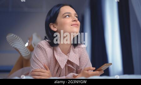 La jeune femme brune rêve couché sur le lit avec un téléphone Banque D'Images