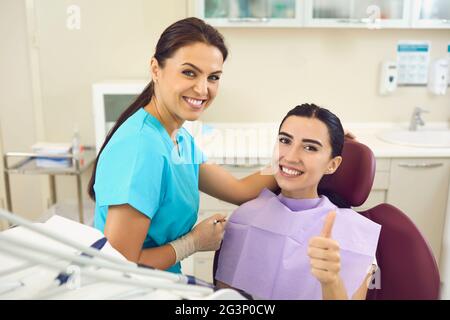 Patient heureux dans la chaise dentaire donnant les pouces et souriant avec dentiste gai à côté Banque D'Images