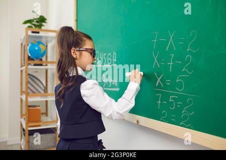 Retour à l'école. Une écolière à lunettes écrit sur un conseil scolaire dans une salle de classe lors d'une conférence. Banque D'Images