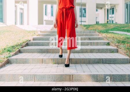 Jeune femme d'affaires méconnaissable vêtue de robe rouge et marchant dans les escaliers. Concept d'entreprise. Banque D'Images