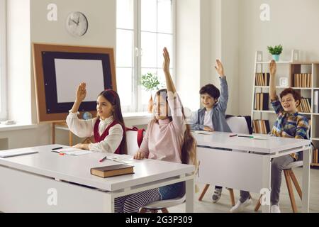 Un groupe d'élèves du primaire lève la main en classe pour répondre aux questions de l'enseignant. Banque D'Images