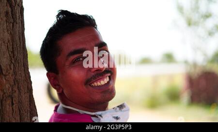 Portrait d'un jeune homme indien souriant avec un arrière-plan fort et clair. Homme asiatique heureux regardant l'appareil photo à l'extérieur. Banque D'Images