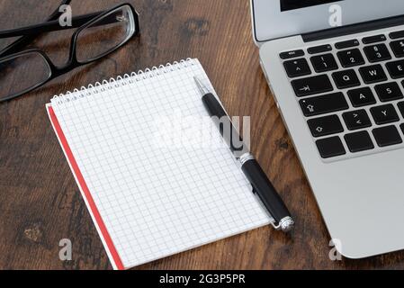 bloc-notes en spirale vierge et stylo avec papier quadrules à côté de l'ordinateur portable sur une table en bois Banque D'Images