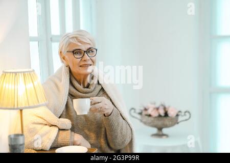 Une femme âgée s'apprécie à la maison et boit du thé Banque D'Images