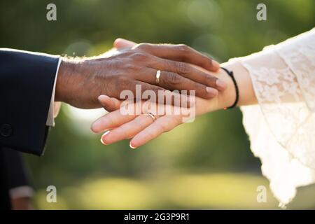 Les mains d'un marié à la peau sombre et d'une mariée à la peau claire avec des anneaux se touchent doucement vue rapprochée Banque D'Images