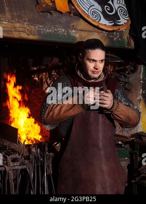 Armes et épées Viking forges dans la forge. Un homme en habits de guerrier est dans la forge sur l'arrière-plan de feu. Banque D'Images