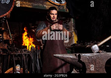 Armes et épées Viking forges dans la forge. Un homme en habits de guerrier est dans la forge sur l'arrière-plan de feu. Banque D'Images