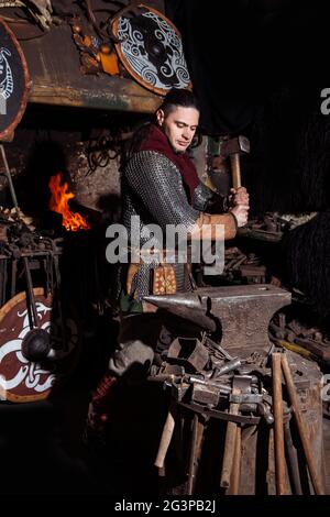 Armes et épées Viking forges dans la forge. Un homme en habits de guerrier est dans la forge sur l'arrière-plan de feu. Banque D'Images