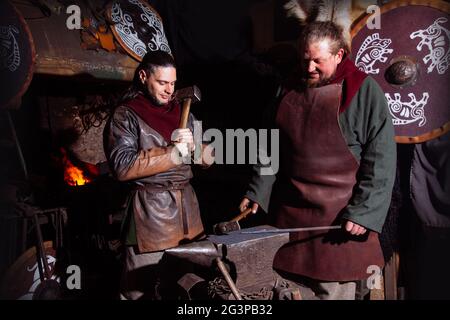 Armes et épées Viking forges dans la forge. Un homme en habits de guerrier est dans la forge sur l'arrière-plan de feu. Banque D'Images