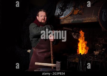 Armes et épées Viking forges dans la forge. Un homme en habits de guerrier est dans la forge sur l'arrière-plan de feu. Banque D'Images