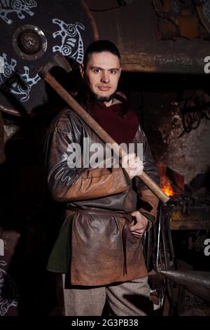 Armes et épées Viking forges dans la forge. Un homme en habits de guerrier est dans la forge sur l'arrière-plan de feu. Banque D'Images