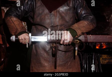 Armes et épées Viking forges dans la forge. Un homme en habits de guerrier est dans la forge sur l'arrière-plan de feu. Banque D'Images