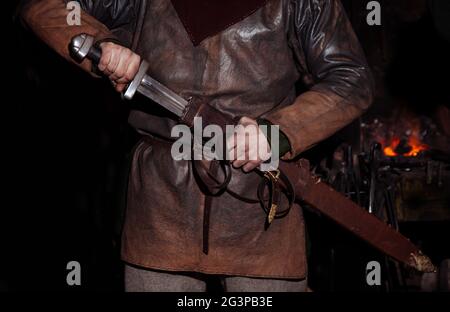 Armes et épées Viking forges dans la forge. Un homme en habits de guerrier est dans la forge sur l'arrière-plan de feu. Banque D'Images