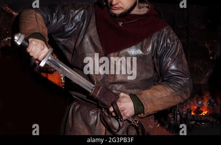 Armes et épées Viking forges dans la forge. Un homme en habits de guerrier est dans la forge sur l'arrière-plan de feu. Banque D'Images