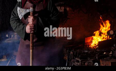 Armes et épées Viking forges dans la forge. Un homme en habits de guerrier est dans la forge sur l'arrière-plan de feu. Banque D'Images