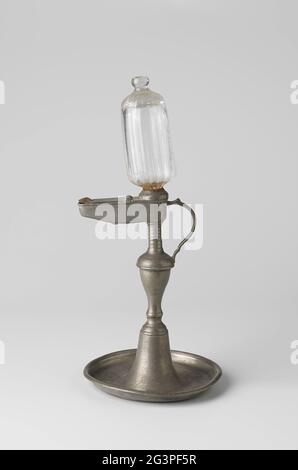 Une lampe à huile en étain avec réservoir en verre. Lampe à huile en étain. La base ronde est dotée d'un bord relevé et fonctionne en forme d'horloge centrale avec une contrainte qui exclut le haut et une lampe à huile porte le bec et la lampe en verre sur une contrainte courte et striée. À l'opposé du bec, la poignée est appliquée juste en dessous de la partie nervurée du coffre. Banque D'Images