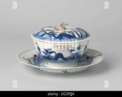 Bol couvert avec support pour femmes dans un paysage. Bol en porcelaine avec demi-oreilles en forme de fleur, peint en bleu sous-glaçure. Sur le bol une représentation continue d'une terrasse clôturée avec deux fois deux dames chinoises (de longues histoires), palmier et banane plante. Le bas est marqué d'une marque à six caractères de l'empereur Kangxi dans un double cercle. Les oreilles ont plus tard été argentées en Europe. Une fissure dans le bord de la cuve. Bleu blanc. Banque D'Images