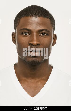 Homme afro-américain attrayant regardant sérieusement l'appareil photo, un homme à la peau sombre dans un t-shirt blanc sur un fond blanc regarde Banque D'Images
