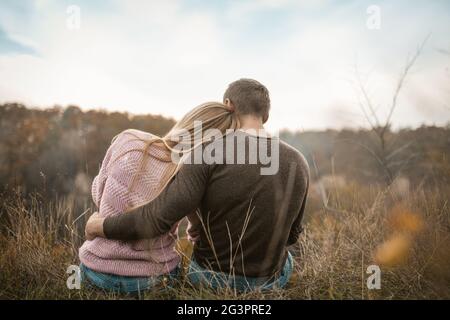 Vue arrière des touristes envoûtants assis sur le bord de la falaise qui inhalent les arômes de la nature d'automne en plein air Banque D'Images