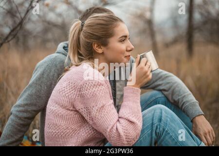 Pique-nique dans la nature. La jeune femme et l'homme se reposent en buvant du café chaud ou du thé tout en s'asseyant sur une couverture à l'herbe d'automne dehors. Profil Banque D'Images