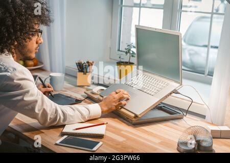 PC portable et tablette graphique jeune designer à la maison. Homme d'affaires arabe travaille de chez lui. Concept freelance Banque D'Images