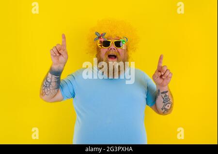 Un homme gras avec une perruque dans la tête et des lunettes de soleil indique quelque chose avec les mains Banque D'Images