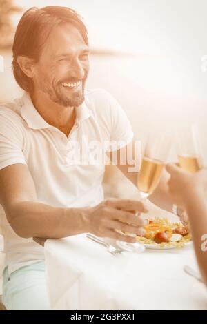 Joyeux homme avec un verre de vin blanc lève des toasts de célébration le jour avec sa femme bien-aimée. Un couple heureux fête son anniversaire de mariage Banque D'Images