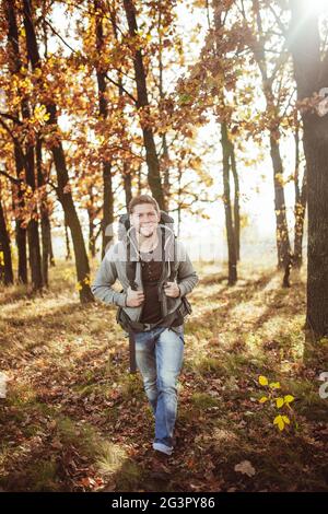 Un jeune homme avec un sac à dos voyage à travers la forêt d'automne lors d'une journée ensoleillée et chaude. Promenades touristiques caucasiennes souriantes dans la nature. Hiki Banque D'Images