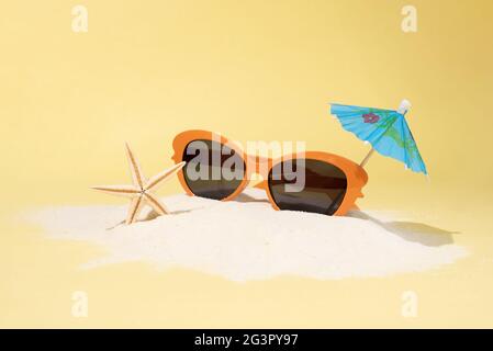 Île de sable avec lunettes de soleil orange, parapluie et étoile de mer sur fond bleu, concept de vacances d'été, gros plan. Banque D'Images