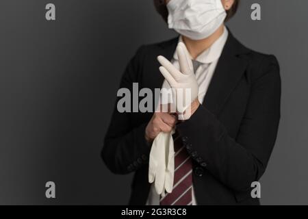 Femme d'affaires dans un masque de protection mettre des gants jetables. Gros plan. Se concentrer sur la main féminine au premier plan. Concept de pandémie Banque D'Images