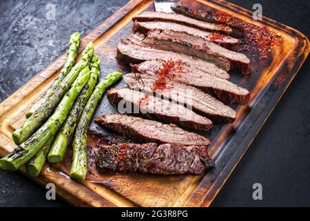Barbecue traditionnel coupé en tranches de bœuf Wagyu vieilli et sec, servi avec des asperges vertes et de la poudre de Chili en gros plan sur un mur rustique Banque D'Images