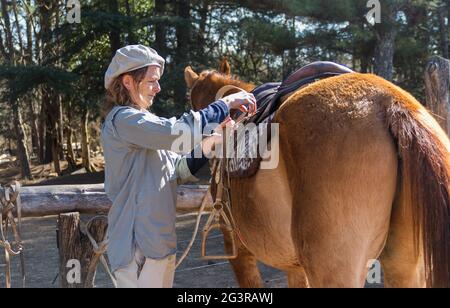 Femme rurale qui selles son cheval sur le terrain Banque D'Images