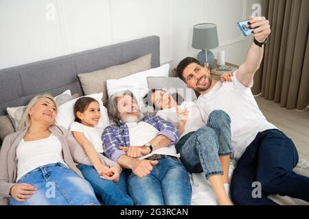 Grand père de famille, mère et grands-parents heureux de plusieurs générations avec une petite petite fille petite-fille qui prend le selfie sur le téléphone portable tout en étant couché sur le lit à la maison. Concept de famille et d'amour Banque D'Images