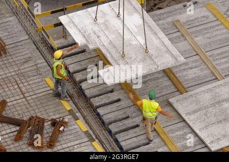 Les travailleurs sur un chantier de construction qui dirige la dalle de béton par une grande grue Banque D'Images